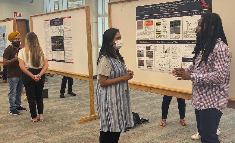 A photo of Jared Barnes (right), a senior biology major from Grenada, talks about his biodegradable drug delivery system research during a poster presentation for the UM Summer Undergraduate Research Group Grant program. Photo by Shea Stewart/UM Office of Research and Sponsored Programs